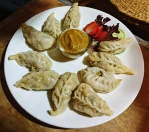 A plate of dumplings with dipping sauce, surrounded by fresh veggies, served on a table.